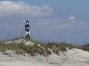 FILE - In this July 9, 2014 file photo, Cape Lookout Lighthouse shines its light over a sand dune from the Atlantic side in New Bern, N.C.  The national seashore in North Carolina invites the public to a climb of the Cape Lookout Lighthouse on New Year's Day. A news release says space is limited and reservations are required.