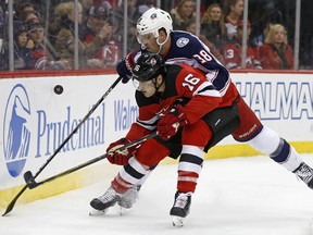 New Jersey Devils defenseman Steven Santini (16) battles for the puck with Columbus Blue Jackets center Boone Jenner (38) during the first period of an NHL hockey game, Friday, Dec. 8, 2017, in Newark, N.J.