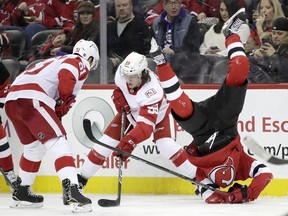 New Jersey Devils center Nico Hischier, right, of Switzerland, flips over while competing for the puck with Detroit Red Wings' Tyler Bertuzzi (59) and Frans Nielsen (51), of Denmark, during the second period of an NHL hockey game, Wednesday, Dec. 27, 2017, in Newark, N.J.