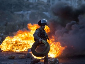 Israeli border police officer clears a burning tire during clashes with Palestinian protesters following protests against U.S. President Donald Trump's decision to recognize Jerusalem as the capital of Israel, in the West Bank city of Ramallah, Saturday, Dec. 9, 2017.