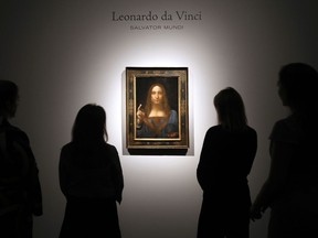 FILE- In this Oct. 24, 2017, file photo, people gather around Leonardo da Vinci's "Salvator Mundi" on display at Christie's auction rooms in London. The rare painting of Christ, which that sold for a record $450 million, is heading to a museum in Abu Dhabi. The newly-opened Louvre Abu Dhabi made the announcement in a tweet on Wednesday, Dec. 6.
