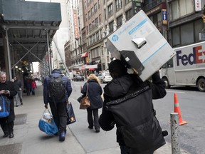 In this Wednesday, Dec. 20, 2017, photo, a delivery man carries a customer order as he leaves the Amazon Prime warehouse in New York.