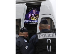 French police officers watch a television set up in a police car and airing a tribute to Johnny Hallyday, outside Johnny Hallyday's house in Marnes-la-Coquette, outside Paris, Wednesday, Dec.6, 2017. Johnny Hallyday, France's biggest rock star for more than half a century and an icon who packed sports stadiums and all but lit up the Eiffel Tower with his pumping pelvis and high-voltage tunes, has died. He was 74.