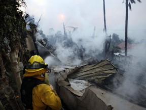 A firefighter hoses down smoldering debris in Ventura, Calif., Tuesday, Dec. 5, 2017. Ferocious Santa Ana winds raking Southern California whipped explosive wildfires Tuesday, prompting evacuation orders for thousands of homes.