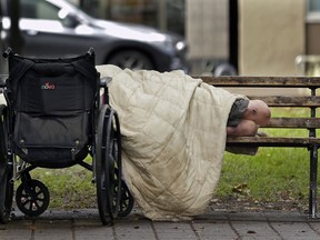 FILE - In this Sept. 19, 2017, file photo, a person sleeps next to a wheelchair on a park bench in downtown Portland, Ore., not far from the city's trendy Pearl District. An annual report found that 80 homeless people died on the streets of Portland and the surrounding area in 2016. The number released Thursday, Dec. 14 is only a slight improvement over 2015, when 88 homeless people died outside.
