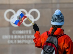 A woman waves a Russian flag outside of the International Olympic Committee (IOC) headquarters in front of the Olympic Rings prior to the opening of the first day of the executive board meeting of the International Olympic Committee (IOC) at the IOC headquarters, in Pully near Lausanne, on Tuesday, Dec. 5, 2017.  Russian athletes will be allowed to compete at the upcoming Pyeongchang Olympics as neutrals despite orchestrated doping at the 2014 Sochi Games, the International Olympic Committee said Tuesday.