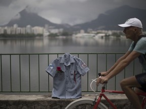 In this Dec. 27, 2017 photo, a man rides his bike past a police uniform shirt, stained in red representing spilt blood, as it hangs on a fence during a demonstration promoted by the NGO Rio de Paz, in Rio de Janeiro, Brazil. 13 uniforms with red roses in their pockets were displayed at Rodrigo de Freitas lagoon, in memory of the 132 police officers killed this year in the state.