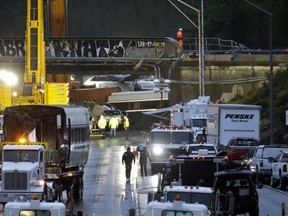 A damaged train car sits on a flatbed trailer at left as work continues to remove other cars at the scene of an Amtrak train crash onto Interstate 5 a day earlier Tuesday, Dec. 19, 2017, in DuPont, Wash.   Federal investigators say they don't yet know why the train was traveling 50 mph over the speed limit when it derailed Monday, killing some people and injuring dozens.
