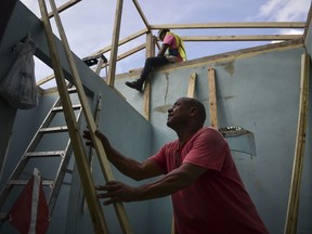 In this Nov. 15, 2017 photo, Pedro Deschamps helps workers hired by FEMA to carry out the installation of a temporary awning roof at his house, which suffered damage during Hurricane Maria, in San Juan, Puerto Rico.  The Department of Homeland Security's internal watchdog says his office will be investigating how a tiny Florida company won more than $30 million in contracts for desperately needed relief supplies following Hurricane Maria. The Associated Press first reported last month that Bronze Star LLC failed to deliver the emergency tarps and plastic sheeting needed to cover tens of thousands of Puerto Rican homes damaged by the storm's winds. The Federal Emergency Management Agency eventually terminated the contracts without paying any money.