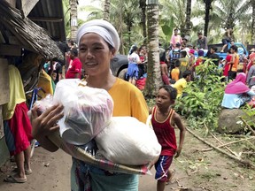 A resident smiles as she walks home with relief supplies being distributed to storm-affected villages of Lanao del Norte Sunday, Dec. 24, 2017 in southern Philippines. Tropical Storm Tembin unleashed flash floods that swept away people and houses and set off landslides in the southern Philippines. (AP Photo)