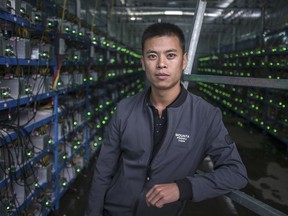 In this Sept. 26, 2016, photo, a Tibetan bitcoin miner poses with his shelves of bitcoin mining computers at a bitcoin mine built beside a hydropower station in a remote valley of Aba prefecture in southwestern China's Sichuan province. The launch of a U.S. futures contract for bitcoin on Sunday, Dec. 10, 2017, underscores the virtual currency's increasing mainstream acceptance, including in many parts of Asia, where it already has a wide following among speculators and investors .(Chinatopix via AP)