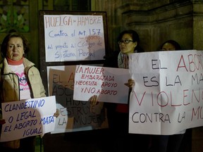 Women hold signs with Spanish messages: "Clandestine or legal, abortion kills all the same," left, and "A pregnant woman needs support not abortion," center below, and "Abortion is the greatest violence against women," far right, on the first day of their hunger strike to protest abortions outside the Cathedral in La Paz, Bolivia, Wednesday, Dec. 6, 2017. Bolivian lawmakers voted on Wednesday to ease the country's tight restrictions on abortions, shrugging aside opposition from religious groups.