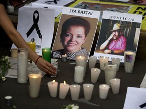 FILE - In this May 16, 2017 file photo, a woman places a candle in front of pictures of murdered journalists Miroslava Breach, left, and Javier Valdez during a demonstration against the killing of journalists, outside the Interior Ministry in Mexico City. More than three dozen Mexican media organizations announced Monday, Dec. 4, 2017 that they are joining forces to try to combat a wave of journalist killings in the country, including at least nine this year.