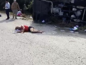 BEST QUALITY AVAILABLE - This video frame shows an injured woman lying on the road next to the overturned bus she was traveling in, in Mahagual, Quintana Roo state, Mexico, Tuesday, Dec. 19 2017. At least 12 people died when the bus carrying cruise ship passengers to Mayan ruins in eastern Mexico flipped over on a highway early Tuesday, officials said. (AP Photo/Stringer)