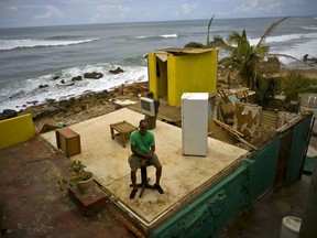 FILE - This Oct. 5, 2017 file photo shows Roberto Figueroa Caballero sitting on a small table in his home that was destroyed by Hurricane Maria in La Perla neighborhood on the coast of San Juan, Puerto Rico. Figueroa put his salvageable items back where they originally were, as if his home still had walls, saying that it frees his mind. A U.N. expert on extreme poverty and human rights is meeting with hurricane victims in Puerto Rico, Monday, Dec. 11.