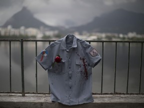 A police uniform shirt, stained in red representing spilt blood, hangs on a fence during a demonstration promoted by the NGO Rio de Paz, in Rio de Janeiro, Brazil, Wednesday, Dec. 27, 2017. 13 uniforms with red roses in their pockets were displayed at Rodrigo de Freitas lagoon, in memory of the 132 police officers killed this year in the state.