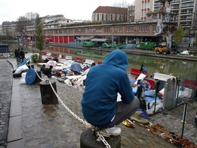 Migrants sit by a makeshift camp in Paris, Thursday, Dec. 21, 2017. The French government is scrambling to meet President Emmanuel Macron's deadline to get migrants off France's streets by year's end.