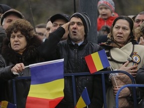 Romanians sing the national anthem during the national day military parade in Bucharest, Romania, Friday, Dec. 1, 2017. Thousands of Romanian troops staged a military parade to celebrate Romania's national day, but key politicians didn't attend, signaling tensions between the president and the ruling left-wing coalition over plans to revamp the justice system.