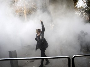 In this Saturday, Dec. 30, 2017 file photo taken by an individual not employed by the Associated Press and obtained by the AP outside Iran, a university student attends a protest inside Tehran University while a smoke grenade is thrown by anti-riot Iranian police, in Tehran, Iran.