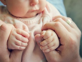 A three-month old baby girl holding the fingers of her father.