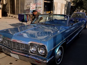 In this Wednesday, Jan. 10, 2018 photo, a man cleans a blue 1964 Chevrolet parked in front of the owner Saad al-Nuaimi's coffee shop in the northern Azamiyah neighborhood of Baghdad, Iraq. The promise of better days after Iraq's victory against the Islamic State group is rekindling interest in vintage cars.