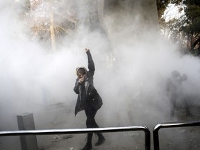 FILE - In this Saturday, Dec. 30, 2017 file photo taken by an individual not employed by the Associated Press and obtained by the AP outside Iran, a university student attends a protest inside Tehran University while a smoke grenade is thrown by anti-riot Iranian police, in Tehran, Iran. Iran has seen its largest anti-government protests since the disputed presidential election in 2009, with thousands taking to the streets in several cities in recent days. Travel restrictions and moves by the government to shut down social media networks have limited the ability of journalists to cover the ongoing unrest, which Iranian state television said has killed 12 people. (AP Photo, File)