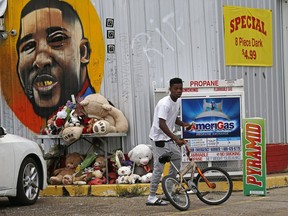FILE - In this June 27, 2017 photo, Ronald Smith gets on his bicycle after stopping at the Triple S Food Mart, where Alton Sterling was shot by police one year ago, in Baton Rouge, La. A year later, visitors routinely stop by the store to photograph the mural of Sterling's smiling face on its aluminum siding. Loved ones of Sterling killed by police and two law enforcement officers, one black, one white, ambushed and killed 12 days later in that city will take part in a discussion on Martin Luther King Jr. Day, Monday, Jan. 15, 2018 in Dallas.