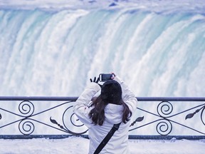 A visitor takes a photograph at the brink of the Horseshoe Falls in Niagara Falls, Ont., as cold weather continues through much of the province on Friday, December 29, 2017. About 14 million people visit the Canadian side of Niagara Falls each year, most of them in the summer months, according to local authorities. But record cold temperatures have turned the natural attraction into a winter wonderland, drawing more visitors this winter than usual, the Niagara Parks Commission says.