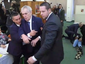 This video frame shows Czech President Milos Zeman, in front, being taken away by security officers as their colleagues, right in the background, interfere with a naked woman shouting at Zeman trying to cast his vote during the presidential election's first round vote in Prague, on Friday, Jan. 12, 2018. Czech Republic's president Milos Zeman and former president of the Czech Academy of Sciences Jiri Drahos are considered as favorites to advance to the runoffs on Januray 26th and 27th.