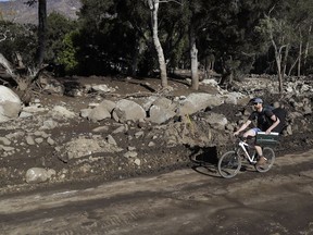 A man rides a bicycle down a road damaged from storms in Montecito, Calif., Friday, Jan. 12, 2018.  The mudslide, touched off by heavy rain, took many homeowners by surprise early Tuesday, despite warnings issued days in advance that mudslides were possible because recent wildfires had stripped hillsides of vegetation that normally holds soil in place.