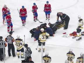 Players from the Montreal Canadiens and Boston Bruins look on as Canadiens' Phillip Danault is tended to by paramedics after he was hit in the head by a puck on a shot by the Bruins' Zdeno Chara during second period of game in Montreal on Saturday.