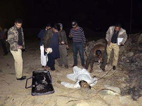 In this Tuesday night, Jan. 16, 2018, photo, Pakistani police officers stand near a body of an attackers in Karachi, Pakistan. Pakistani police say a senior officer known for leading raids on militant hideouts escaped assassination when a suicide bomber riding on a motorcycle blew himself up near his vehicle in the port city of Karachi.