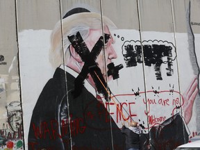 FILE - In this Dec. 7, 2017 file photo, a Palestinian defaces a painting on the separation barrier of U.S. President Donald Trump, with a warning that Vice President Mike Pence is not welcome, in Bethlehem, West Bank. Palestinian Christians say Pence's brand of evangelical Christianity, with its fervent embrace of modern-day Israel as fulfilment of biblical prophecy, lacks their faith's compassion and justice, including for those who have endured half a century of Israeli occupation.