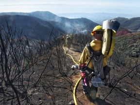 FILE - In this Dec. 19, 2017 file photo provided by the Santa Barbara County Fire Department, Santa Barbara County Firefighters haul dozens of pounds of hose and equipment down steep terrain below E. Camino Cielo to extinguish smoldering hot spots in Santa Barbara, Calif. Evacuations have been ordered for communities below hillsides charred by California's largest-ever wildfire as the first major winter storm of the season brings rare rain and raises the risk of mudslides.