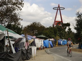 FILE - In this Sept. 14, 2017 file photo a cyclist passes the row of tents and tarps along the Santa Ana riverbed near Angel Stadium in Anaheim, Calif. Orange County officials are putting hundreds of homeless camped out along the dusty riverbed near Angel Stadium on notice: they have to move out starting in two weeks. Formal notices were posted at the encampment on Monday, Jan. 8, 2018, said Carrie Braun, a spokeswoman for the county sheriff's department.