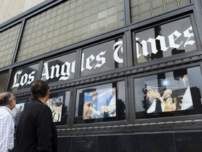 FILE - In this May 16, 2016 file photo passersby look at news photos posted outside the Los Angeles Times building downtown Los Angeles. Los Angeles Times journalists have voted to unionize for the first time in the paper's 136-year history. The National Labor Relations Board on Friday, Jan. 19, 2018, announced results of a Jan. 4 newsroom vote.