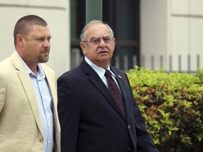 In this March 31, 2016 photo, Iberia Parish Sheriff Louis Ackal, center, leaves the U.S. District Courthouse in Lafayette, La., after being arraigned as part of an ongoing U.S. Justice Department Civil Rights Division investigation of the Iberia Parish Sheriff's Office.   A federal trial involving a man who was fatally shot while handcuffed has been delayed amid new allegations that a Louisiana sheriff used racial slurs and instructed deputies how to cover up "illegal actions" against arrested suspects. U.S. Magistrate Judge Patrick Hanna agreed Tuesday, Jan. 30, 2018, to postpone the trial involving a lawsuit filed by relatives of Victor White III. The 22-year-old man had his hands cuffed behind his back when he died in the rear of an Iberia Parish Sheriff's Office patrol car in March 2014. In a court filing Monday, lawyers for White's family said two former employees of the sheriff's office recently contacted them with "highly critical and important information" about Sheriff Ackal.