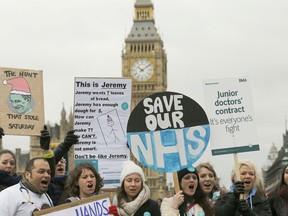 FILE - In this Wednesday, Feb. 10, 2016 file photo, Junior National Health Service (NHS) doctors wave placards referring to British Conservative Party Secretary of State for Health, Jeremy Hunt, during a protest outside St Thomas Hospital in London. This winter has brought a daily drip of grim stories from Britain's health care system, and experts say alarm bells should be ringing across the entire system.