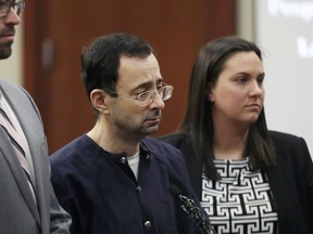 Larry Nassar walks to the podium with attorneys Matt Newburg, left, and, Shannon Smith during his sentencing hearing Wednesday, Jan. 24, 2018, in Lansing, Mich.  The former sports doctor who admitted molesting some of the nation's top gymnasts for years was sentenced Wednesday to 40 to 175 years in prison as the judge declared: "I just signed your death warrant."  The sentence capped a remarkable seven-day hearing in which scores of Nassar's victims were able to confront him face to face in the Michigan courtroom.