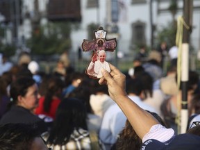 A vendor hawks souvenir crosses featuring an image of Pope Francis as faithful gather outside the Apostolic Nunciature to get a glimpse of the pontiff, in Lima, Peru, Friday, Jan. 19, 2018. Francis is expected to meet with several thousand indigenous people gathering in a coliseum in Puerto Maldonado, the city considered a gateway to the Amazon, in the first full day of the pontiff's visit to Peru.