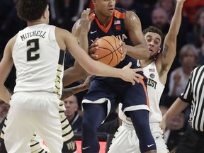 Virginia's Devon Hall, center, looks to pass as Wake Forest's Mitchell Wilbekin, back, and Donovan Mitchell, front, defend during the first half of an NCAA basketball game in Winston-Salem, N.C., Sunday, Jan. 21, 2018.