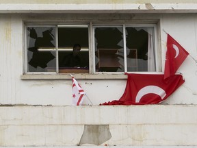 A police officer is seen through a brocket window of the Afrika newspaper office with Turkish flags, right, and Turkish Cypriot breakaway flag after it was attacked by supporters of the Turkish President Recep Tayyip Erdogan in the Turkish occupied northern part of the divided capital Nicosia, Cyprus, Monday, Jan. 22, 2018.  Editor of afrika, Sener Levent alleged during an interview with The Associated Press that Monday's attack was prompted by Turkish President Recep Tayyip Erdogan.