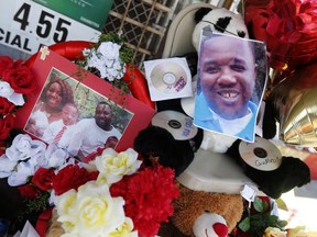 FILE - In this July 7, 2016 file photo, photos of Alton Sterling are interspersed with flowers and mementos at a makeshift memorial in front of the Triple S Food Mart in Baton Rouge, La.  A deadly confrontation between two white Louisiana police officers and Sterling lasted less than 90 seconds. The criminal investigation of Alton Sterling's fatal shooting by one of the officers has lasted more than a year-and-a-half _ and there's no clear end in sight.