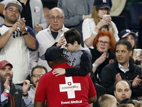 FILE - In this May 24, 2017, file photo, fans applaud as a medical employee carrying an injured youngster from the stands after the boy was hit in the head by a piece of New York Yankees's Chris Carter's bat that split during the seventh inning of a baseball game against the Kansas City Royals at Yankee Stadium in New York. The Yankees are expanding netting to protect seats behind each dugout and for five sections past down both foul lines, a decision announced after several fans were injured last year.