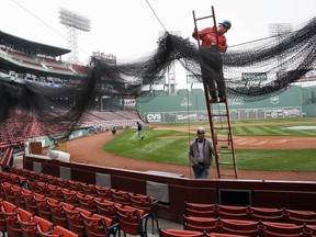 FILE - In an April 2, 2009 file photo, Local 7 ironworkers Kevin McConologue, on ladder, and Scott White put protective netting in place over the seating behind home plate at Fenway Park in Boston. Boston Red Sox president Sam Kennedy announced Saturday, Jan. 20, 2018 that the team is planning what he calls a "dramatic" expansion of safety netting at Fenway Park.  He says the netting will be extended past the dugouts on both the left field and right field lines.