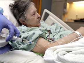 In this Monday, Jan. 8, 2018, photo, a nurse administers an I.V. push of antibiotics to Alice McDonald at ProMedica Toledo Hospital in Toledo, Ohio. A nasty flu season is hitting U.S. hospitals already scrambling to maintain patient care amid severe shortages of crucial sterile fluids, particularly saline solution needed to administer I.V. medicines and rehydrate patients.