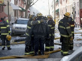 In this Saturday, Jan. 6, 2018, photo, firefighters embrace as their colleagues battle a row home fire in Philadelphia. A veteran firefighter was fatally injured Saturday when a burning row home collapsed in Philadelphia and he became pinned under the debris, authorities said. A person who lived in the home was also killed.