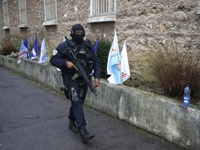 A hooded police officer patrols outside the Fresnes prison with unions flags along the wall, and where Jawad Bendaoud is expected to be jailed, outside Paris, Wednesday Jan.24, 2018. The trial of Bendaoud, accused of providing assistance to the suspected ringleader of the Paris attacks could be disrupted by prison guards protesting their working conditions.