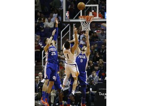 Phoenix Suns guard Devin Booker (1) has his shot altered by Philadelphia 76ers forward Dario Saric (9) and guard Ben Simmons (25) during the first half of an NBA basketball game, Sunday, Dec. 31, 2017, in Phoenix.