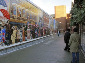 In this Wednesday, Jan. 3, 2018 photo, pedestrians view a mural in downtown Burlington, Vt. The city is considering options to make the art more inclusive after an activist defaced its plaque and said the mural is racist.